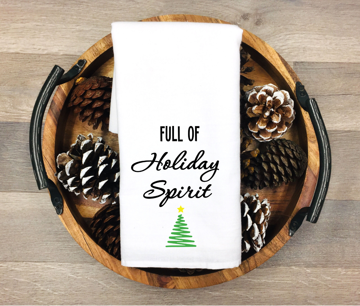 Decorative towel with 'Full of Holiday Spirit' text and pinecones on a wooden tray.